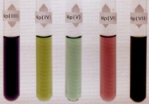 Oxidační stavy neptunia a jejich zbarvení. Od Los Alamos National Lab. (http://www.chemie-master.de/pse/pse.php?modul=Np) [Public domain], prostřednictvím Wikimedia Commons
